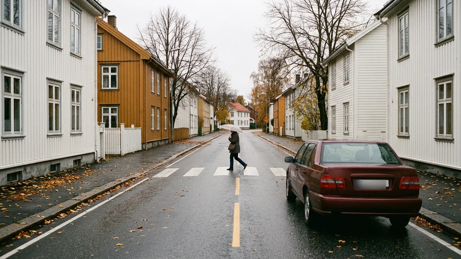 En bil har stanset foran et gangfelt i en rolig bygate mens en fotgjenger krysser fra venstre mot høyre.