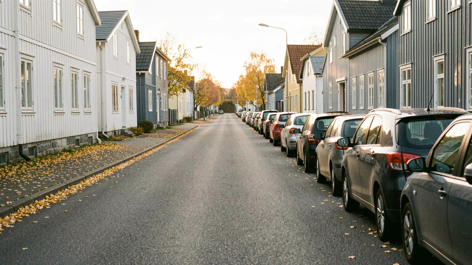 En rolig boliggate om høsten med biler parkert på høyre side, tett inntil fortauskanten og i kjøreretningen.