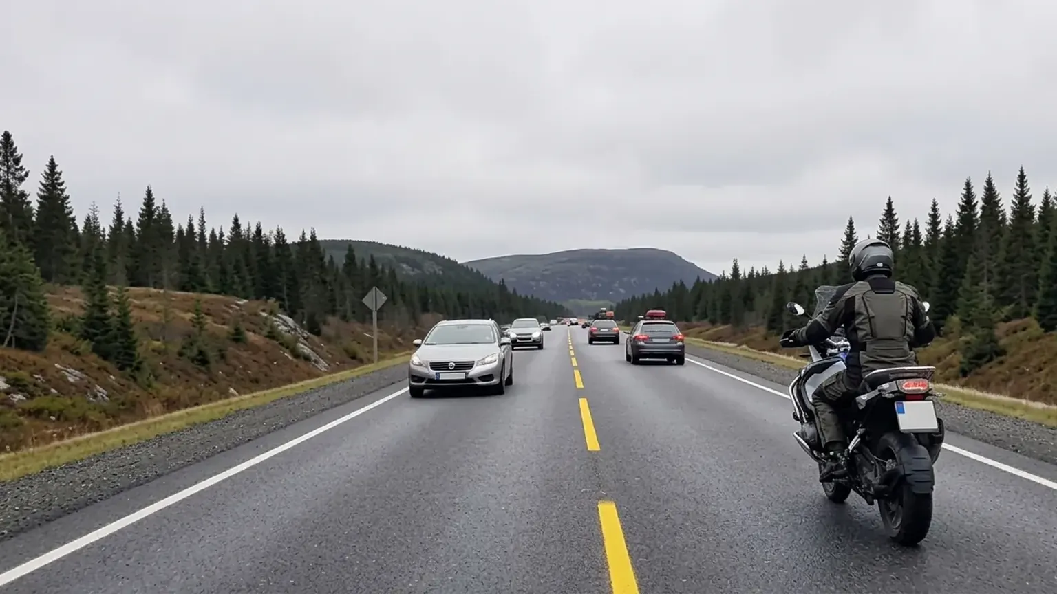 En motorsyklist med lys på kjører i høyre felt på en tofelts vei, mens møtende biler passerer på den andre siden av den gule midtlinjen.